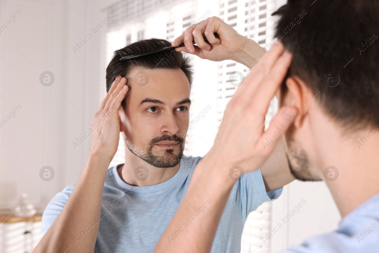 Photo of Handsome man styling his hair with comb near mirror at home