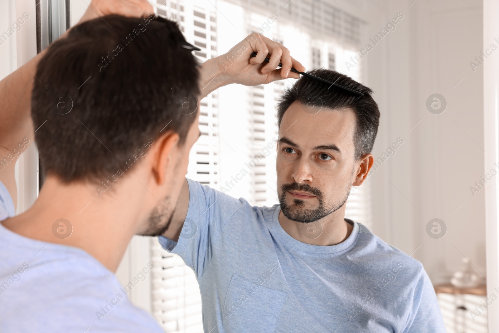 Photo of Handsome man styling his hair with comb near mirror at home