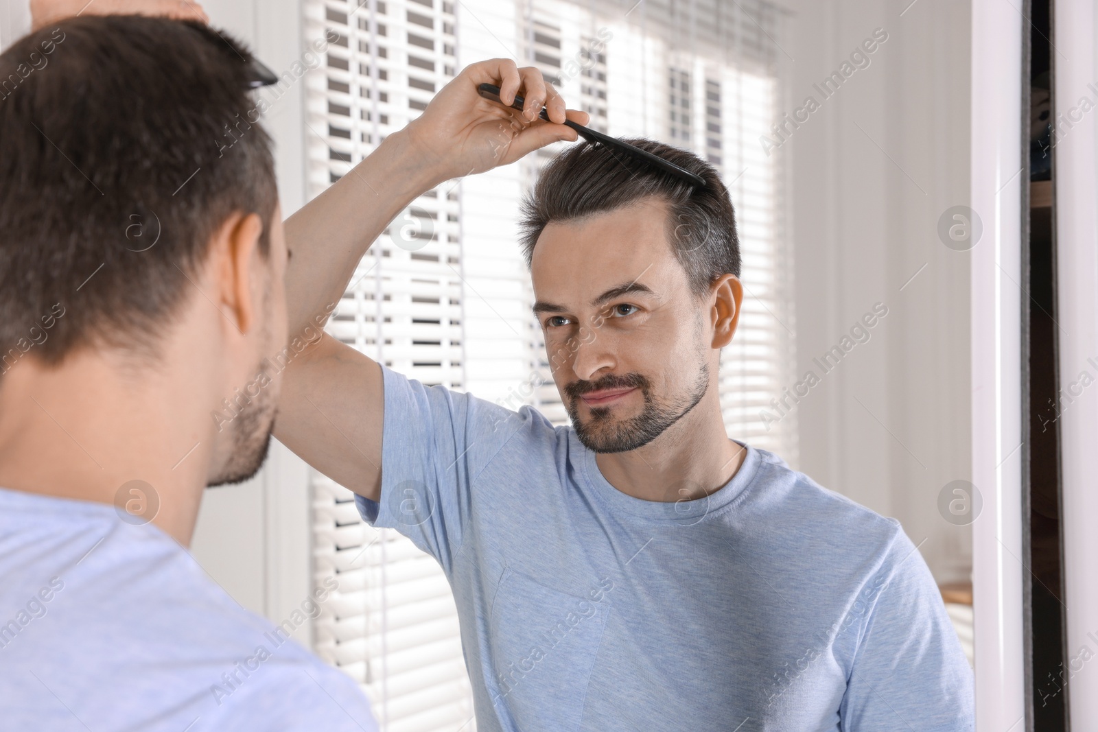 Photo of Handsome man styling his hair with comb near mirror at home