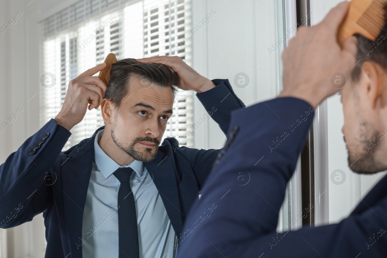 Photo of Handsome man styling his hair with comb near mirror at home