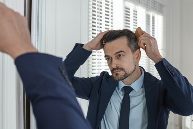 Photo of Handsome man styling his hair with comb near mirror at home