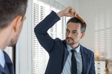 Photo of Handsome man styling his hair with comb near mirror at home