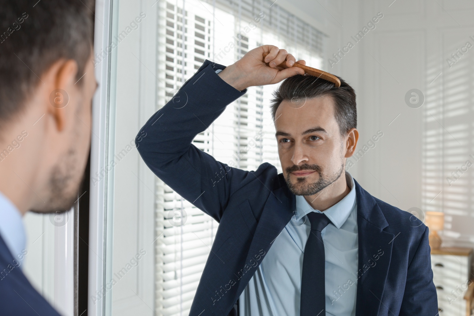 Photo of Handsome man styling his hair with comb near mirror at home