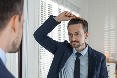 Photo of Handsome man styling his hair with comb near mirror at home