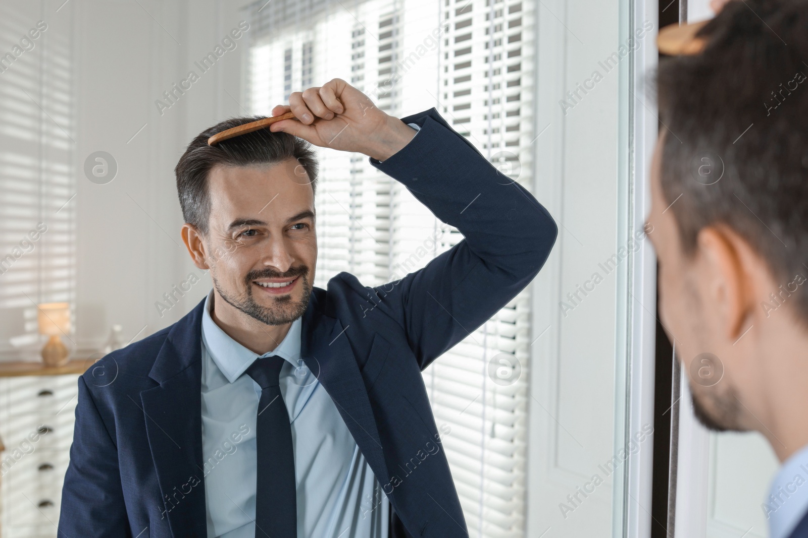 Photo of Handsome man styling his hair with comb near mirror at home