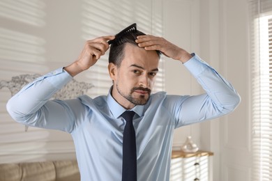 Photo of Handsome man combing his hair at home