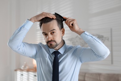 Photo of Handsome man combing his hair at home