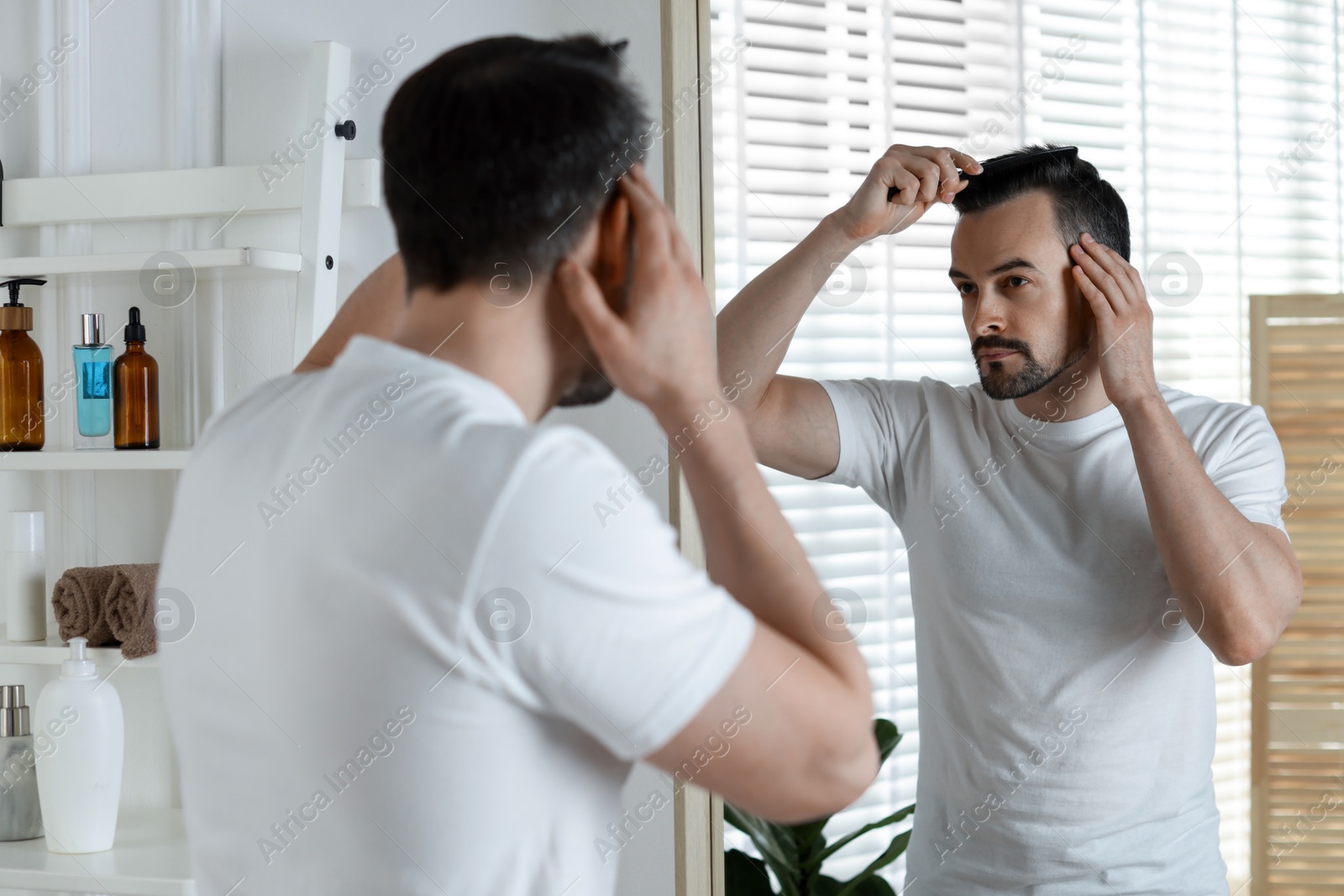 Photo of Handsome man styling his hair with comb near mirror at home