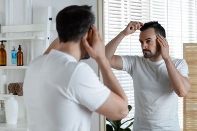 Handsome man styling his hair with comb near mirror at home