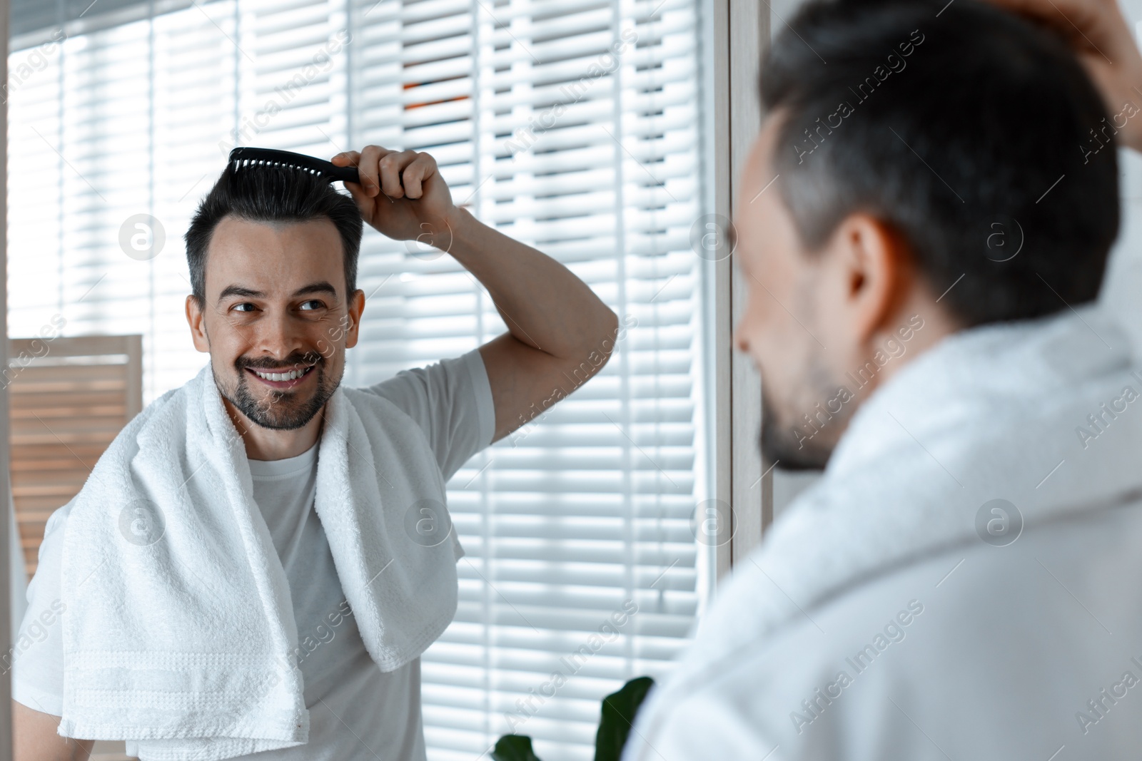 Photo of Handsome man styling his hair with comb near mirror at home