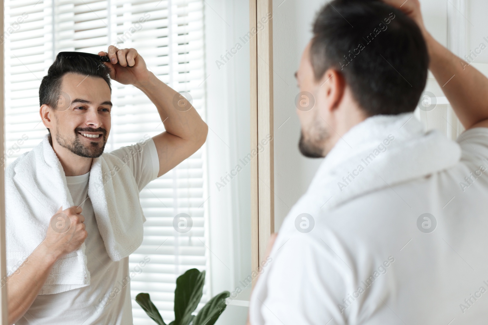 Photo of Handsome man styling his hair with comb near mirror at home