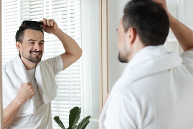 Photo of Handsome man styling his hair with comb near mirror at home