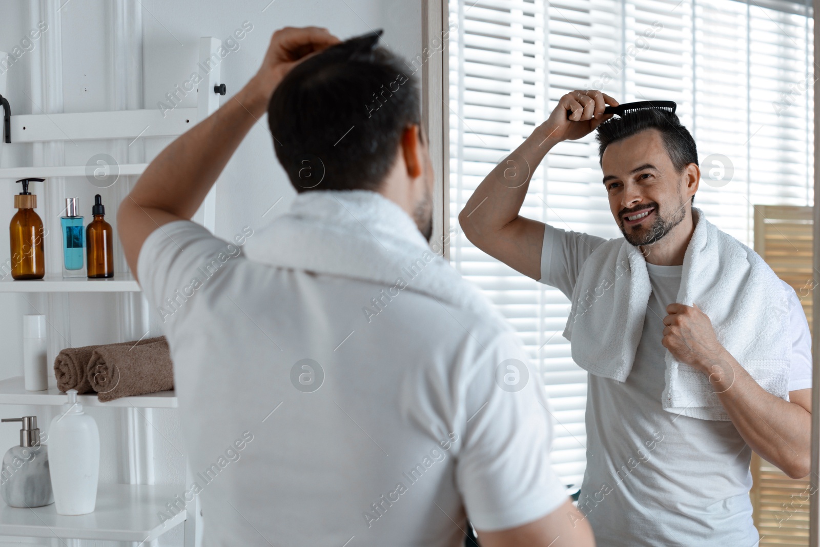 Photo of Handsome man styling his hair with comb near mirror at home