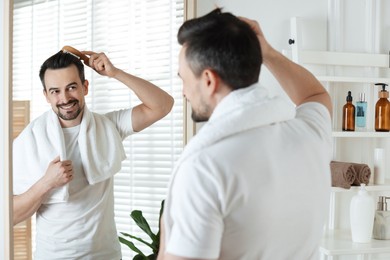 Photo of Handsome man styling his hair with comb near mirror at home