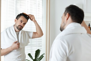 Photo of Handsome man styling his hair with comb near mirror at home