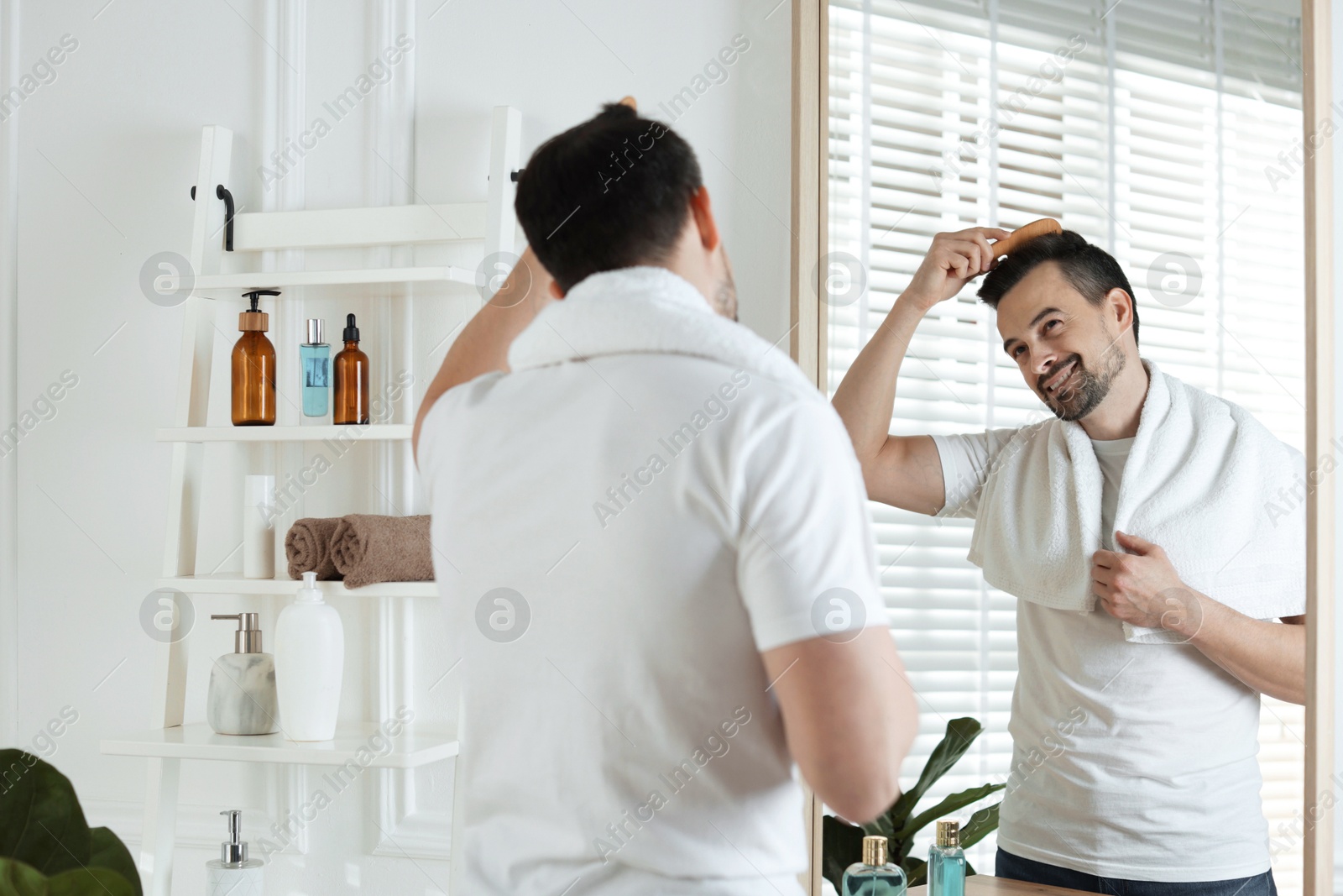 Photo of Handsome man styling his hair with comb near mirror at home