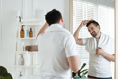 Photo of Handsome man styling his hair with comb near mirror at home