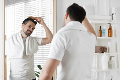 Photo of Handsome man styling his hair with comb near mirror at home