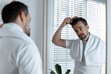 Photo of Handsome man styling his hair with comb near mirror at home