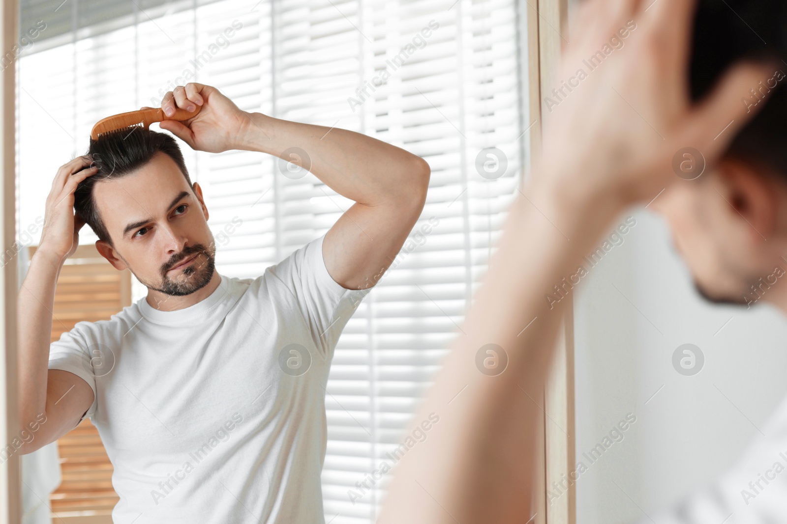 Photo of Handsome man styling his hair with comb near mirror at home