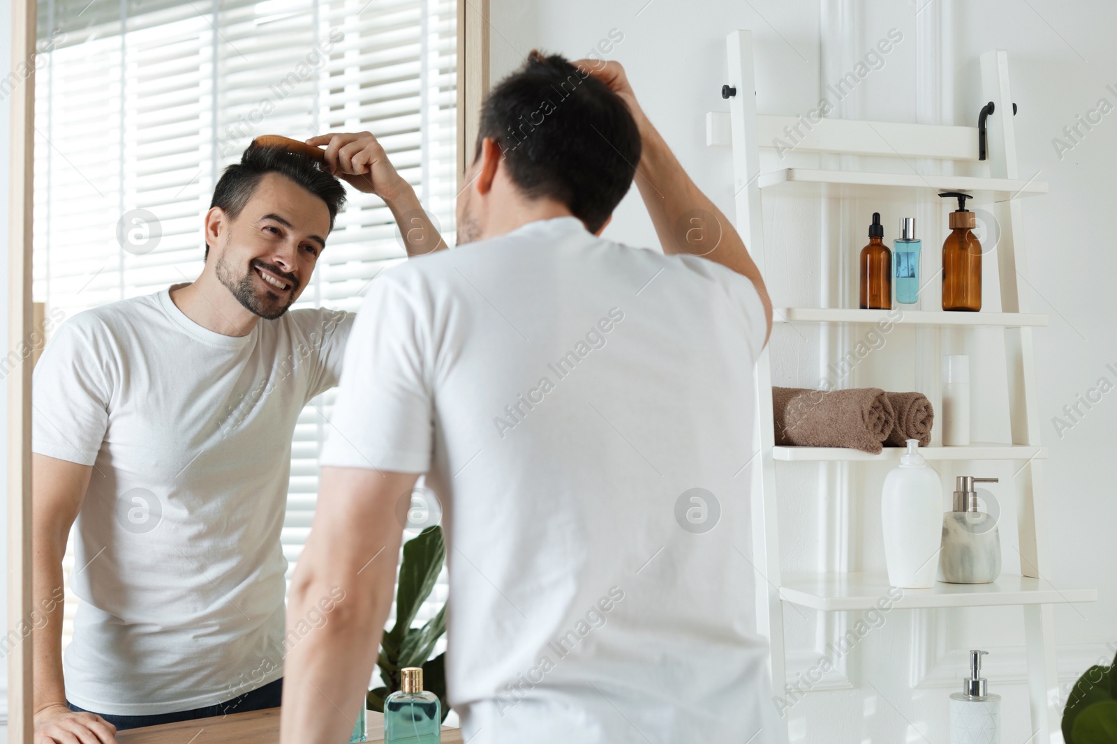 Photo of Handsome man styling his hair with comb near mirror at home