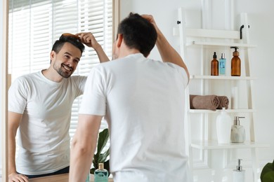 Photo of Handsome man styling his hair with comb near mirror at home