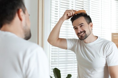 Photo of Handsome man styling his hair with comb near mirror at home