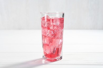 Photo of Sweet soda water with ice cubes in glass on white wooden table, closeup