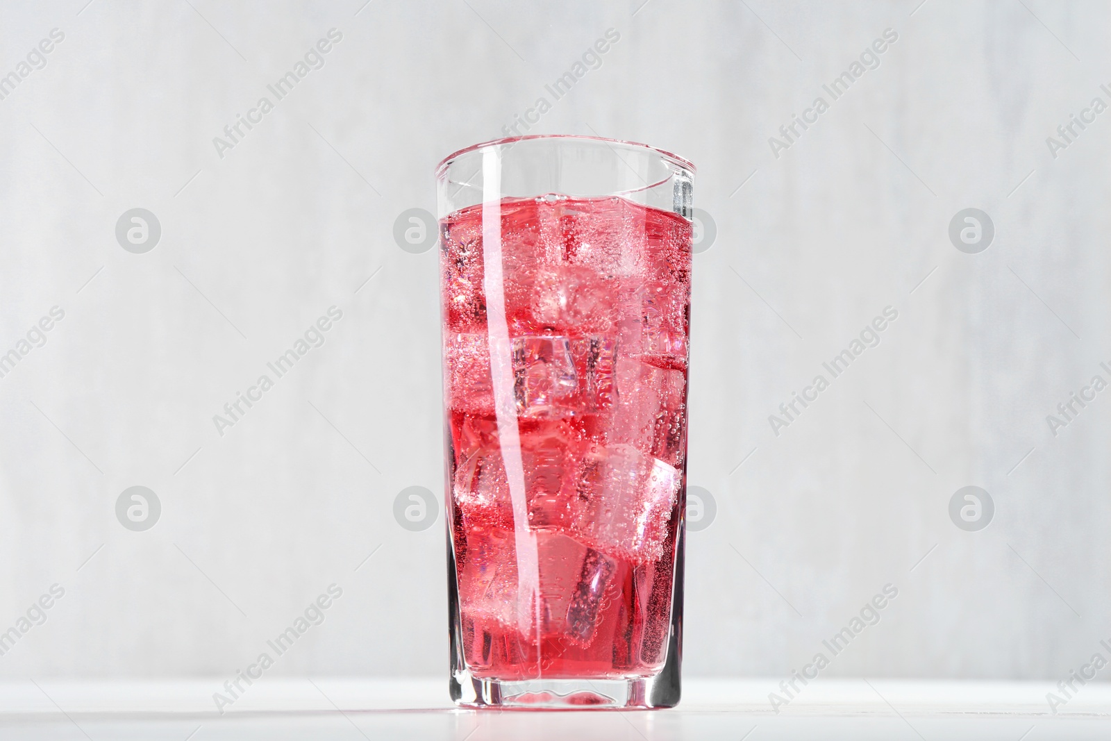 Photo of Sweet soda water with ice cubes in glass on white table, closeup