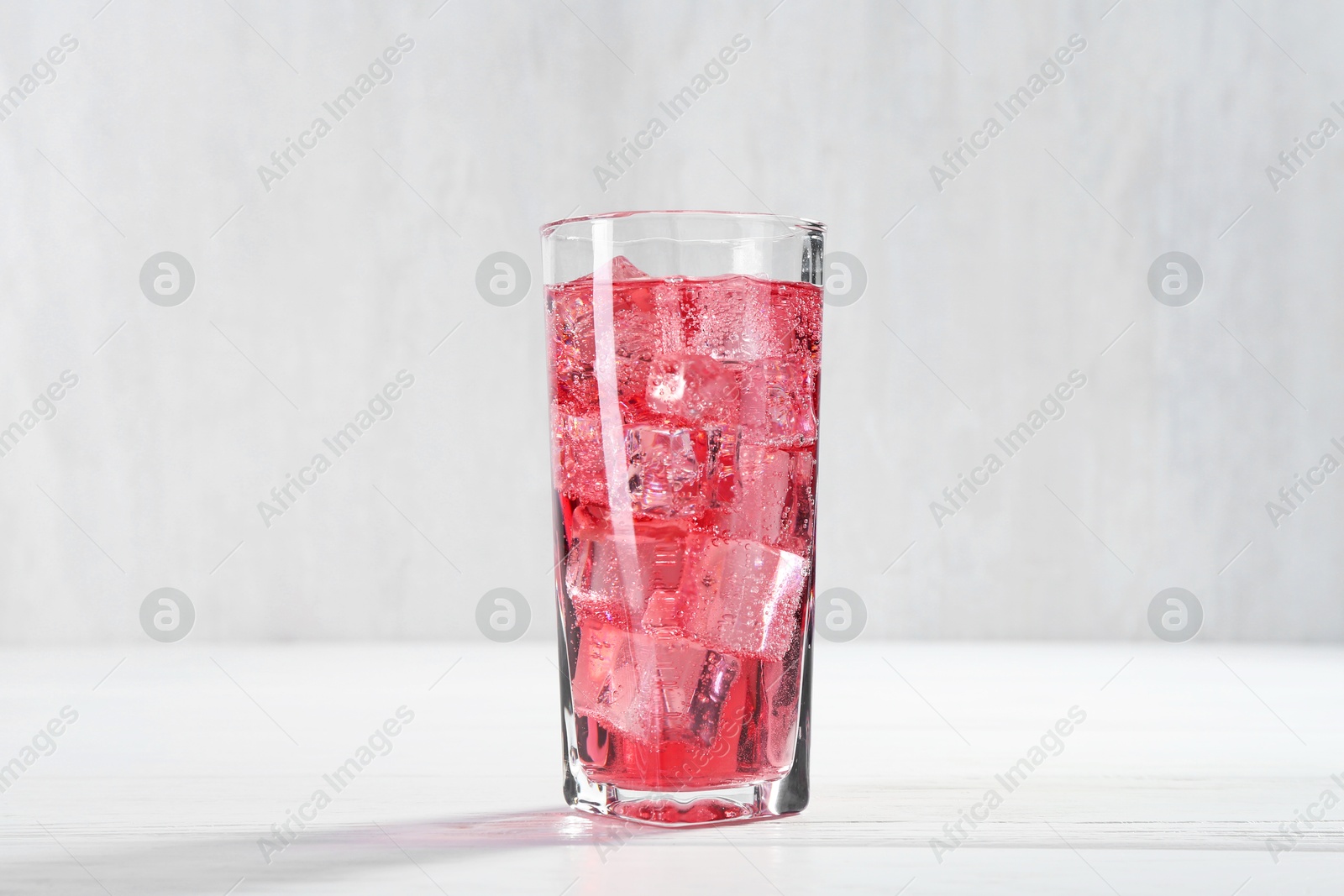 Photo of Sweet soda water with ice cubes in glass on white wooden table