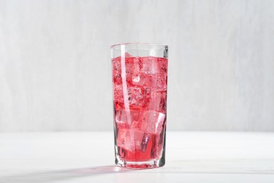 Photo of Sweet soda water with ice cubes in glass on white wooden table