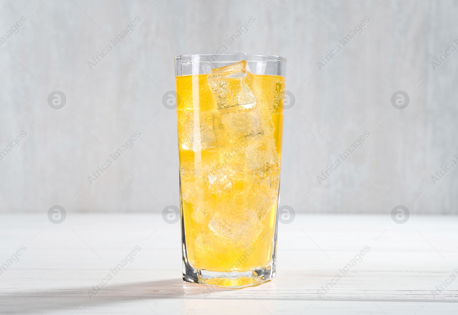 Photo of Sweet soda water with ice cubes in glass on white wooden table