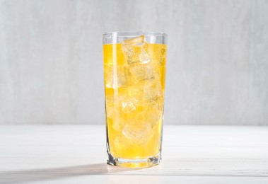 Photo of Sweet soda water with ice cubes in glass on white wooden table