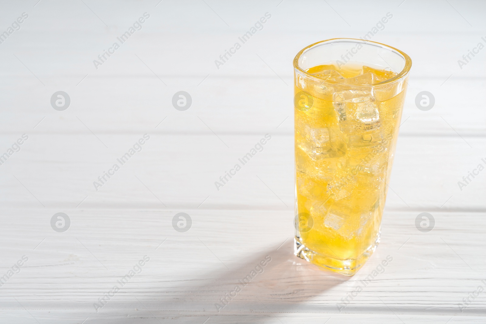 Photo of Sweet soda water with ice cubes in glass on white wooden table, space for text