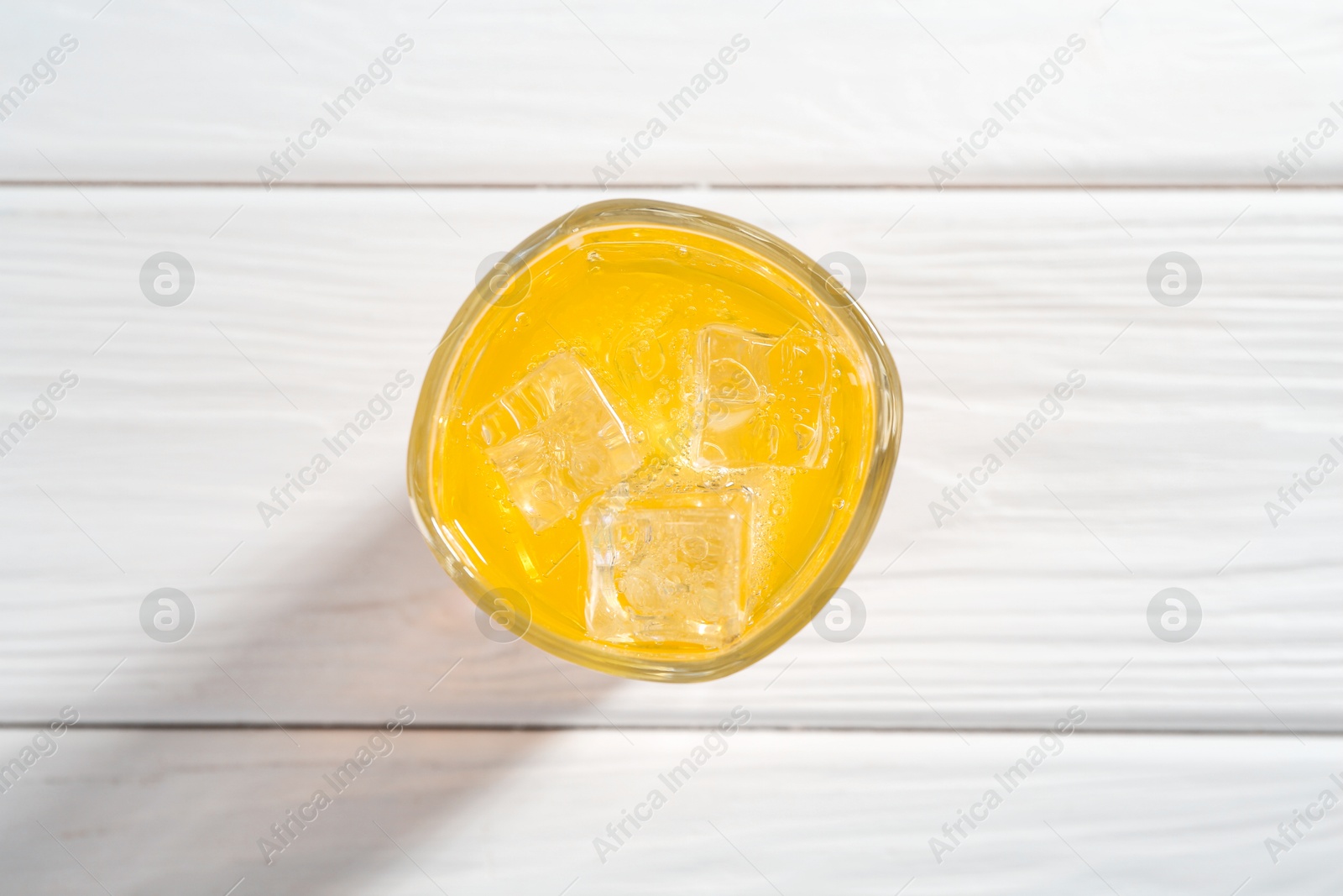 Photo of Sweet soda water with ice cubes in glass on white wooden table, top view