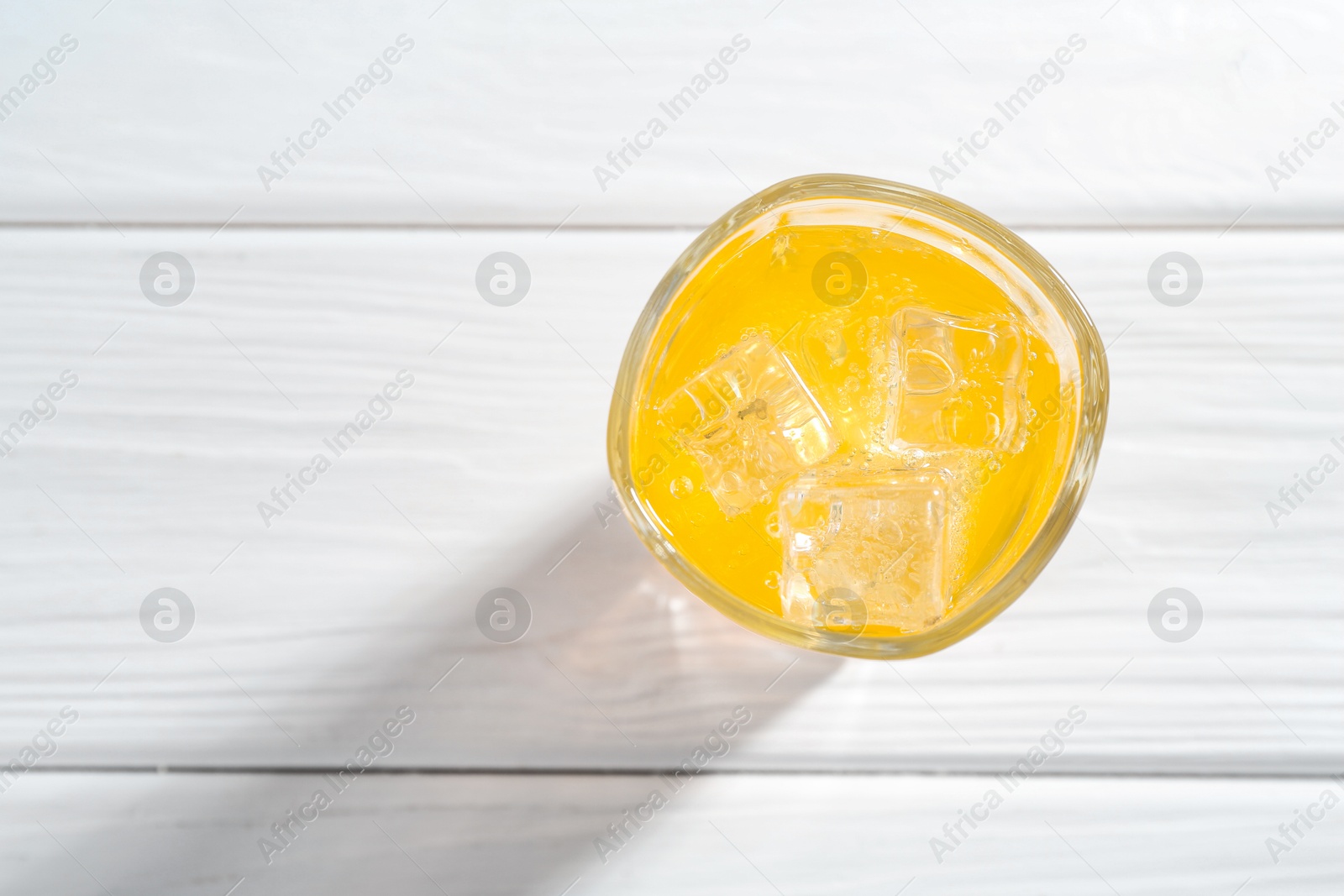 Photo of Sweet soda water with ice cubes in glass on white wooden table, top view. Space for text