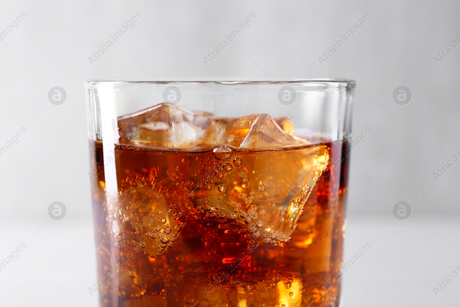 Photo of Sweet soda water with ice cubes in glass on blurred background, closeup