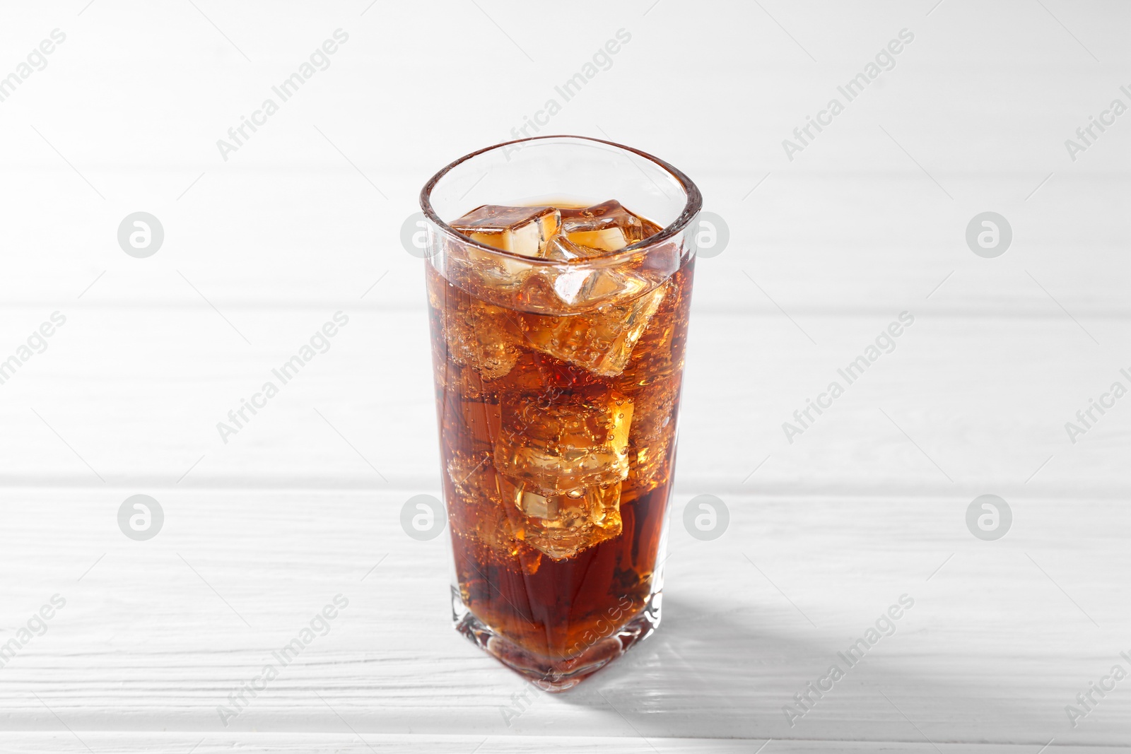 Photo of Sweet soda water with ice cubes in glass on white wooden table, closeup