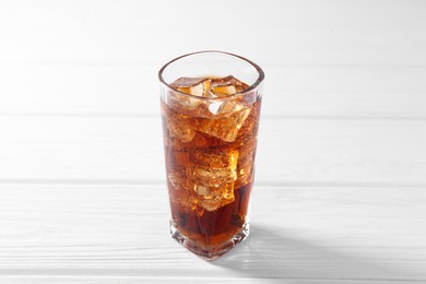 Photo of Sweet soda water with ice cubes in glass on white wooden table, closeup