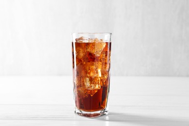 Photo of Sweet soda water with ice cubes in glass on white wooden table