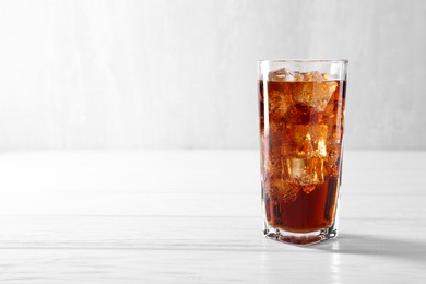 Photo of Sweet soda water with ice cubes in glass on white wooden table, space for text