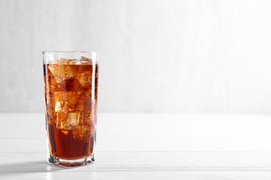 Photo of Sweet soda water with ice cubes in glass on white wooden table, space for text