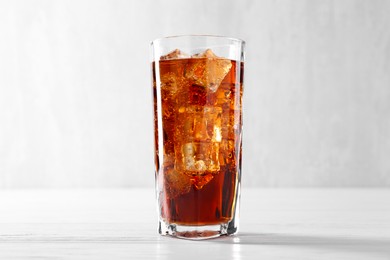 Photo of Sweet soda water with ice cubes in glass on white wooden table, closeup