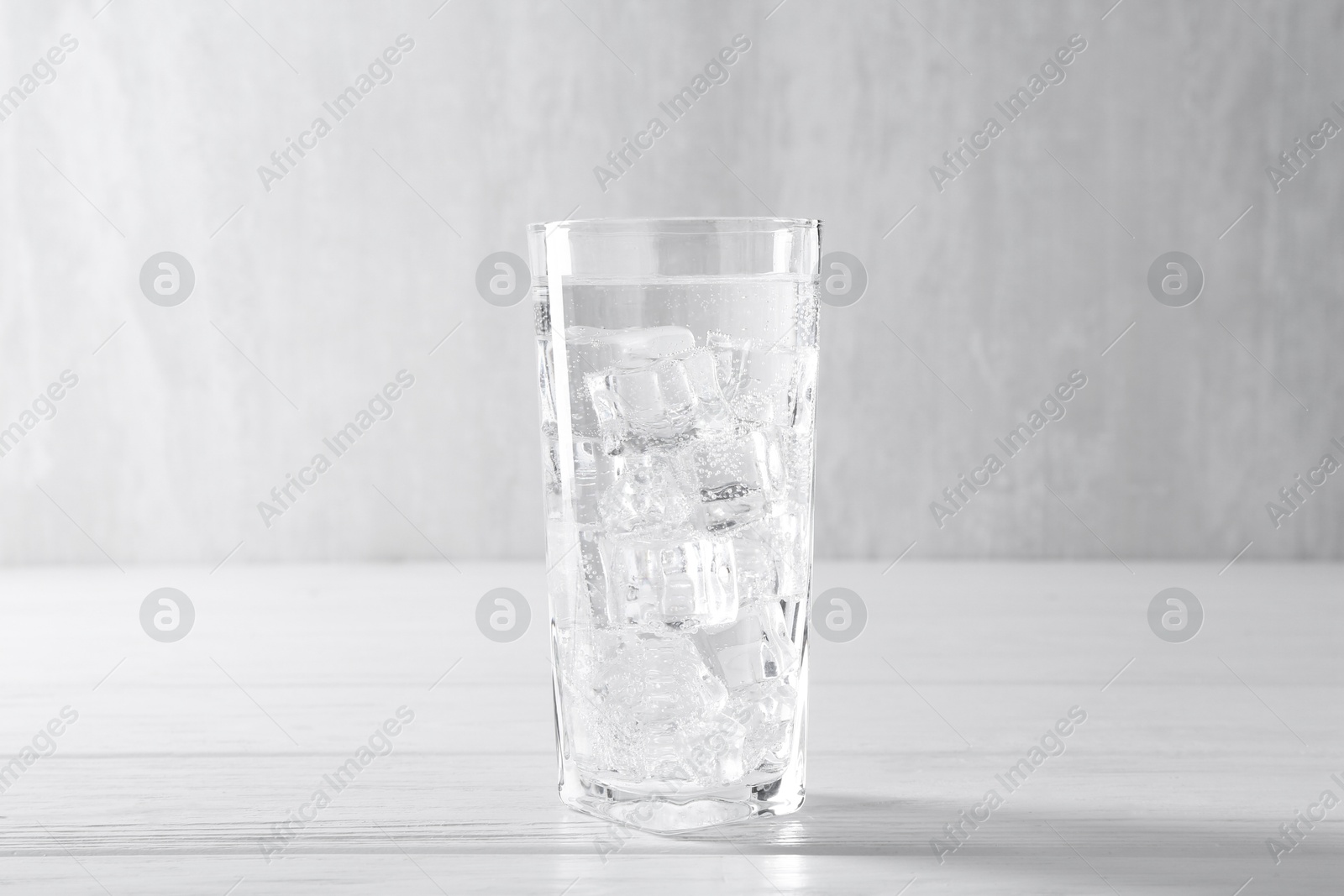 Photo of Refreshing soda water with ice cubes in glass on white wooden table