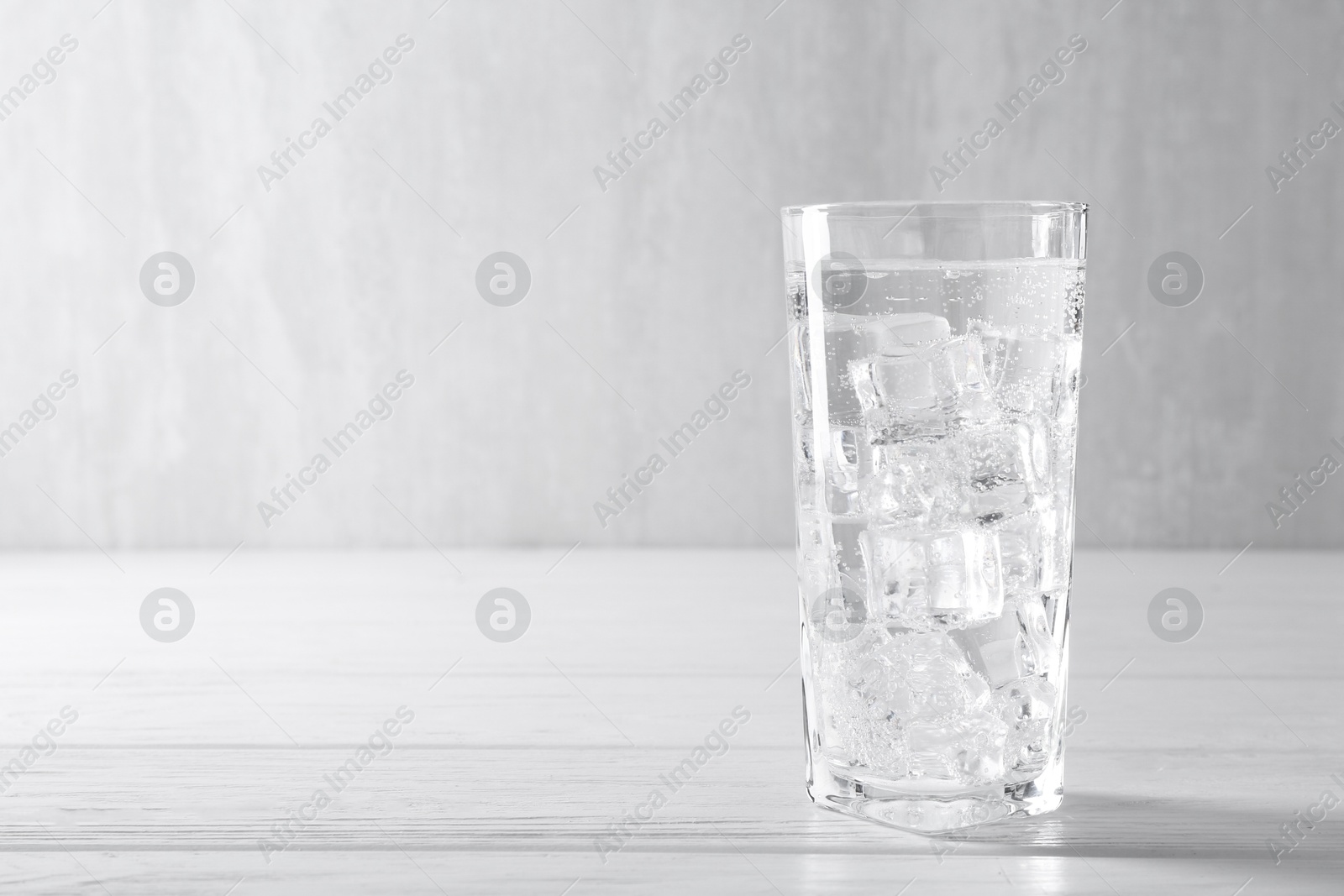 Photo of Refreshing soda water with ice cubes in glass on white wooden table, space for text