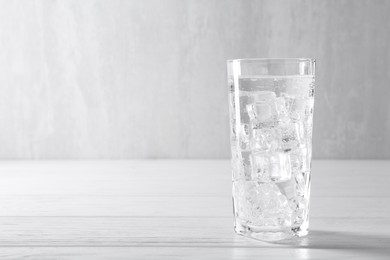 Photo of Refreshing soda water with ice cubes in glass on white wooden table, space for text