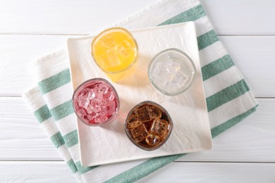 Photo of Soda water of different flavors with ice cubes in glasses on white wooden table, top view