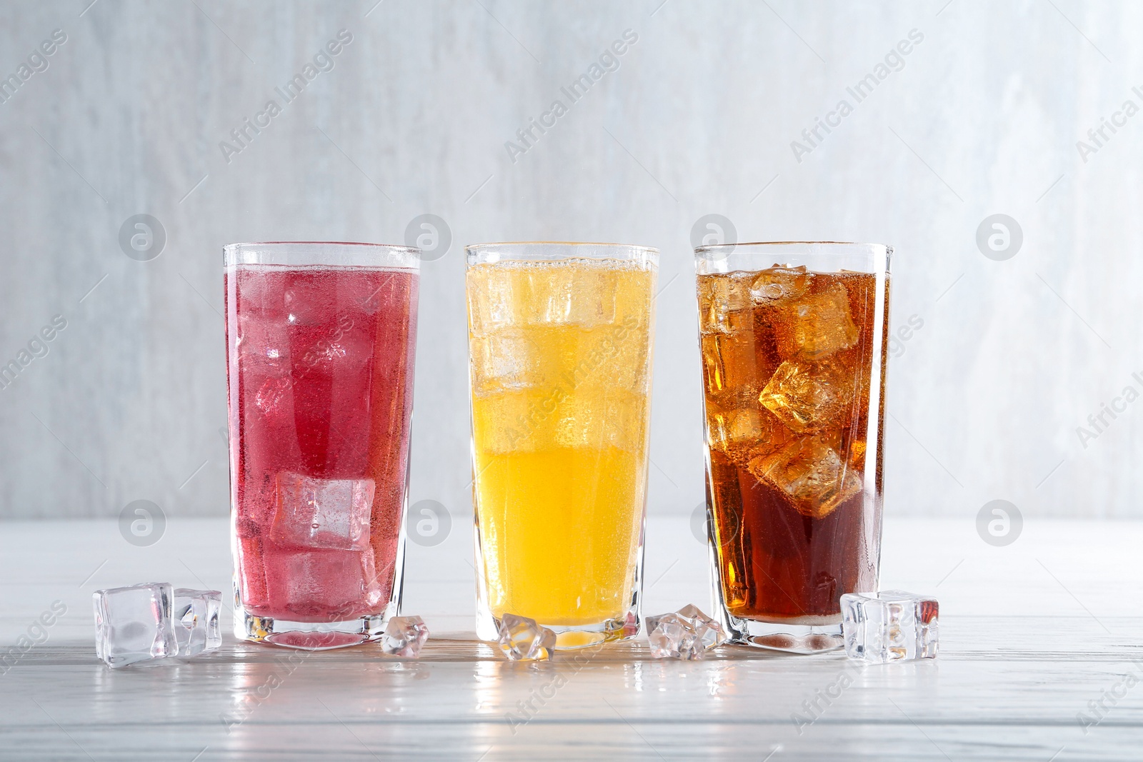 Photo of Soda water of different flavors in glasses with ice cubes on white wooden table