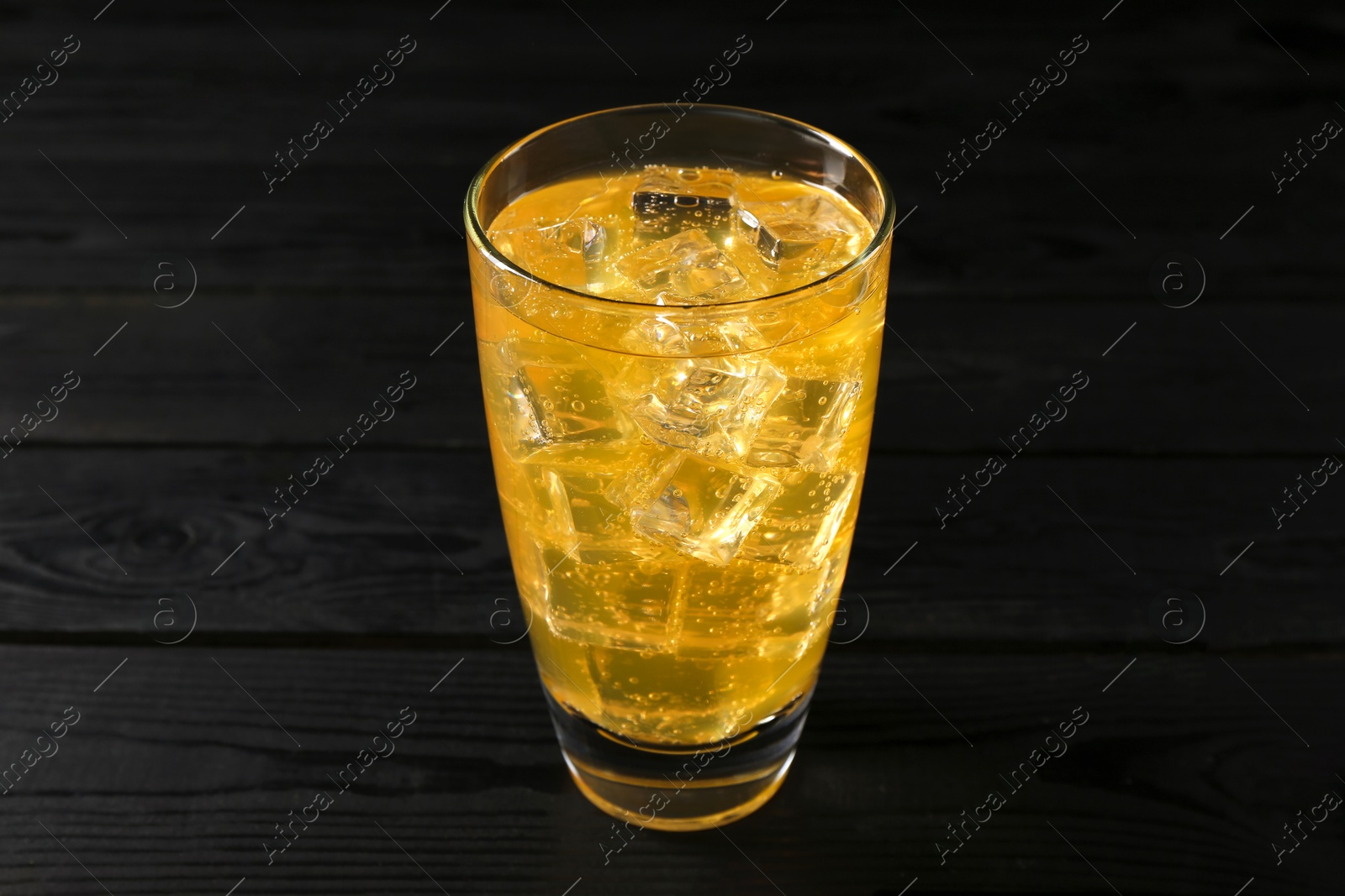 Photo of Sweet soda water with ice cubes in glass on black wooden table