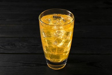 Photo of Sweet soda water with ice cubes in glass on black wooden table